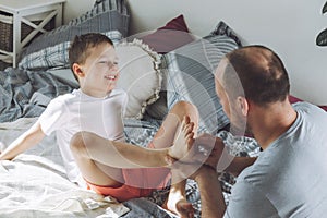 Father plays with his son 7-10 on bed. Dad tickles kids feet. Family, having fun