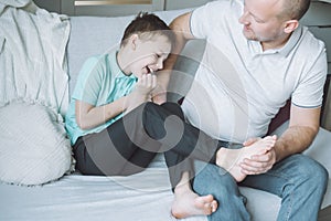 Father plays with his son 7-10 sitting on couch. Dad tickles kids feet. Family, having fun