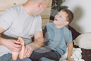 Father plays with his son 7-10 sitting on floor. Dad tickles kids feet. Family, having fun