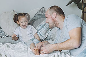 Father plays with little daughter 2-4 on bed. Dad tickles kids feet. Family, having fun