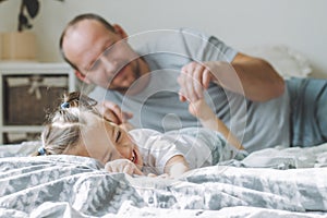 Father plays with little daughter 2-4 on bed. Dad tickles kids feet. Family, having fun