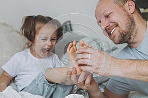 Father plays with little daughter 2-4 on bed. Dad tickles kids feet. Family, having fun