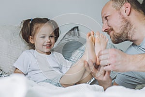 Father plays with little daughter 2-4 on bed. Dad tickles kids feet. Family, having fun