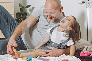 Father plays with little daughter 2-4 on floor. Dad tickles kids feet. Family having fun