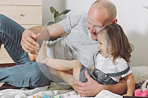 Father plays with little daughter 2-4 on floor. Dad tickles kids feet. Family having fun