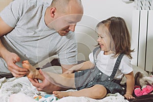 Father plays with little daughter 2-4 on floor. Dad tickles kids feet. Family having fun