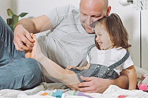 Father plays with little daughter 2-4 on floor. Dad tickles kids feet. Family having fun