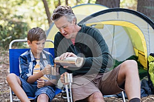 Father pouring drink in cup for son in forest