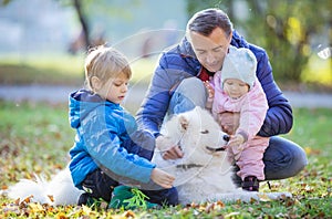 Father with preschool son and baby daugther playing with samoyed dog in park