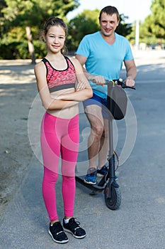 Father and preteen daughter riding kick scooter