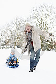 Father Pulling Son On Sledge Through Snow