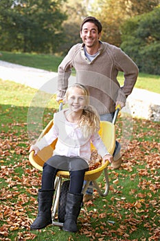 Father pushing child through autumn leaves