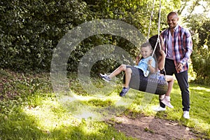 Father Pushing Children On Tire Swing In Garden