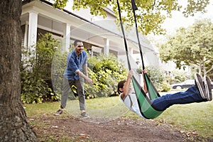 Father Pushing Daughter On Garden Swing At Home