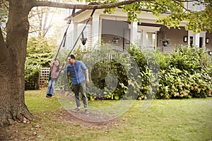 Father Pushing Daughter On Garden Swing At Home