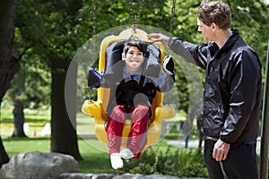 Father pushing disabled boy in special needs swing photo