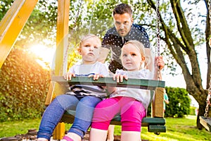 Father pushing his daughters on swing in a park.