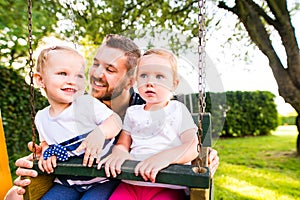 Father pushing his daughters on swing in a park.