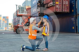 Father puts a safety helmet on little daughter at Container cargo site. Business heir concept. Happy father wearing safety helmet