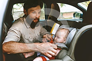 Father putting baby in safety car seat happy family