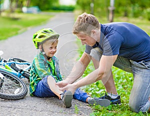 Father putting band-aid on young boy's injury who fell off his b