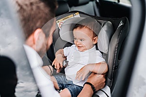 Father putting one year old baby in child car seat and smiling. Lifestyle concept