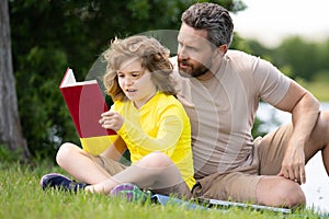 Father read a book with son in a park outdoors. Father and child son reading outdoor on green nature background. Dad