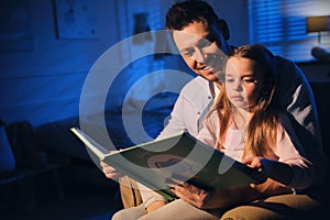 Father reading bedtime story to daughter at home