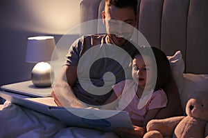 Father reading bedtime story to daughter at home