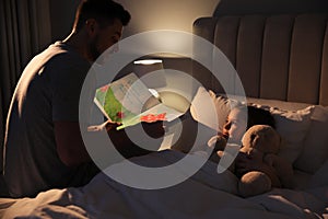 Father reading bedtime story to his daughter at home