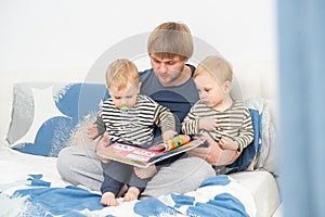 father reading a book to his sons twins on bed at home, spending time together