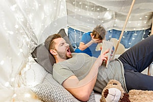 Father reading book to scared little son in blanket fort