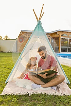 Father reading a story to his daughter while camping in the backyard