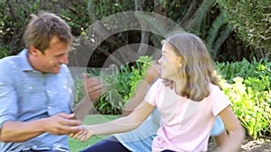 Father Resting In Garden As Daughters Jump On Him