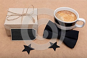 Father`s Day Background. Cup of coffee, beautiful present and black bow tie on brown background flat lay. Fathers day.