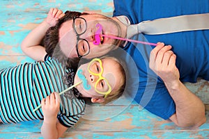 Father`s day concept. Happy father and son in eyeglasses lying on the blue floor background, top view portrait. Happy dad and son