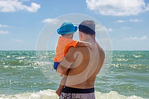 Father`s day. dad holds toddler in his arms against the backdrop of sea waves rear view close-up