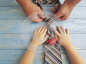 father`s day hands dad and child heart tie on blue wooden background