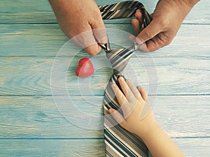 father`s day hands dad and child holding heart tie on blue wooden background