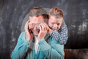 Father& x27;s day. Happy little kid boy hugging dad while close eyes. Father and son. Child is making surprise