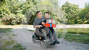 father's day. little cute boy sits on his father's lap with gifts in his hands. a man is a person with disability