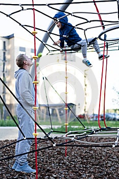 Father`s day a man watches a little boy play merrily on a modern European city playground