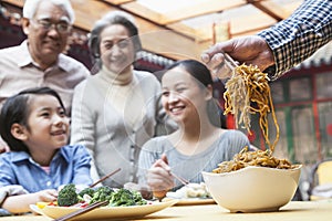 Father serving noodles with chopsticks at a family dinner