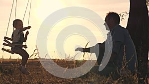 Father shakes his little daughter on a swing in the glare of the sun, dad and kid play samlet at sunset, soar in the air