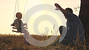 Father shakes his little daughter on a swing in the glare of the sun, dad and kid play samlet at sunset, soar in the air