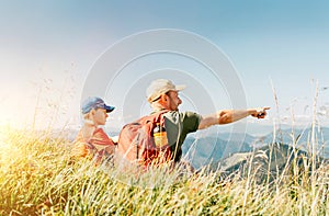 Father showing something interesting to his teenager son sitting on the grass during their mounting hiking walking