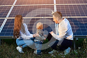 Father shows his family the solar panels on the plot near the house during a warm day