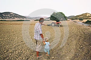 Father shows his toddler son an old tractor on a plowed field among hills. Countryside in Cyprus