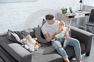 father sitting on couch and feeding baby daughter from bottle in