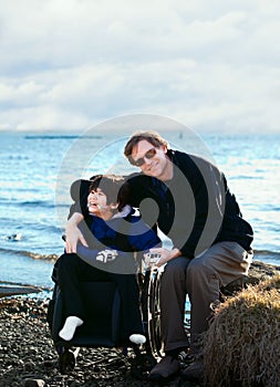 Father sitting with disabled son along lake shore